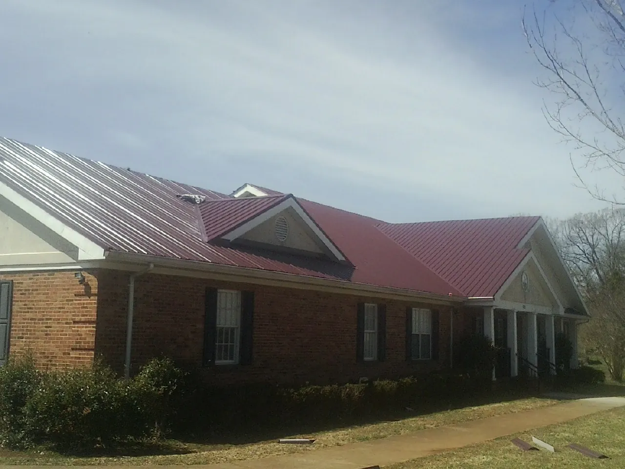 Red metal roof with gabled entries on a long brick building, from a Hail Damage Roof Repair job in Sidman