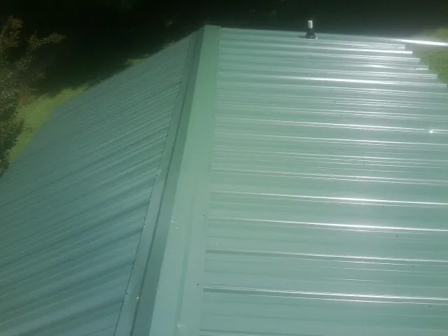 New green metal panels meeting at the ridge of a roof — Flat Roof Repair work by our crew in Sidman