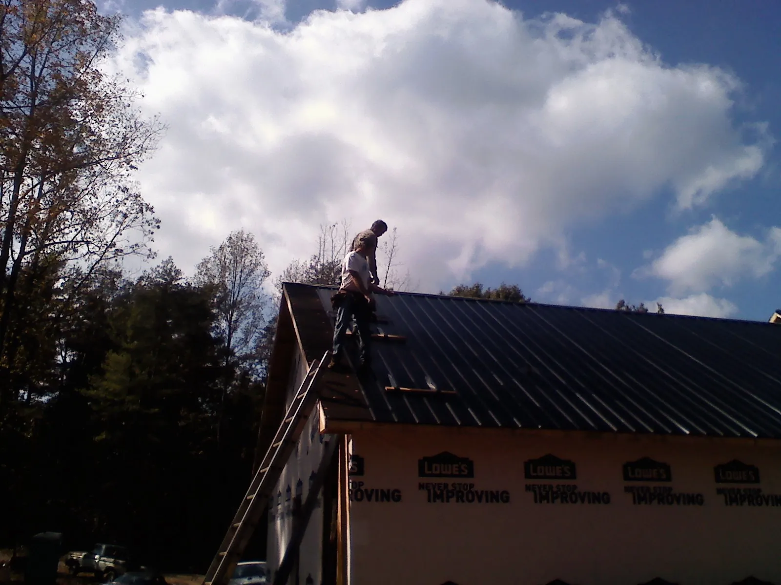 Roofer fastening dark metal panels high against a cloudy sky in Sidman