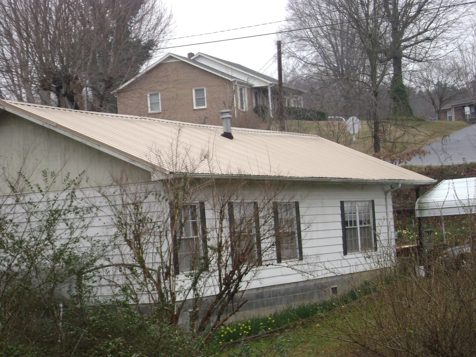 Tan metal roof on a white sided house set into a hillside — Commercial Roofing by Roofing Brothers in Sidman