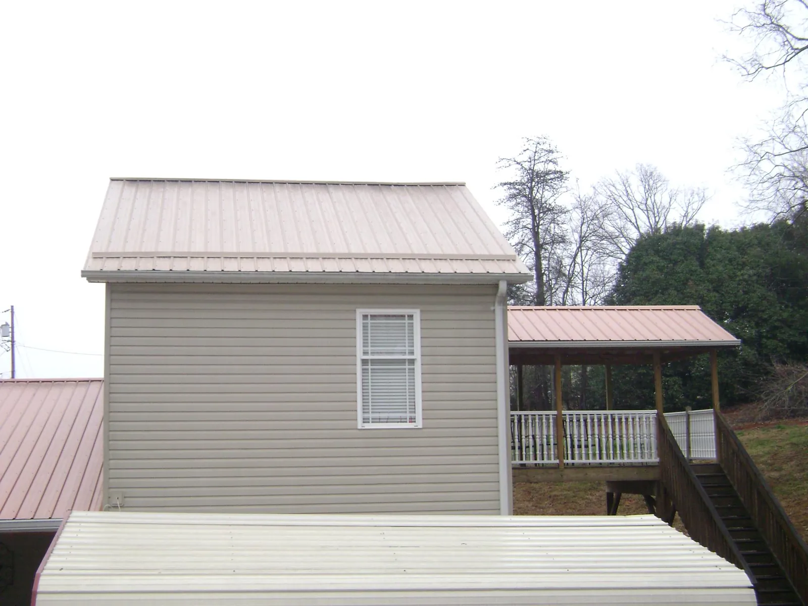 Tan metal roofs on a two story addition and attached porch, from a Roof Replacement job in Sidman